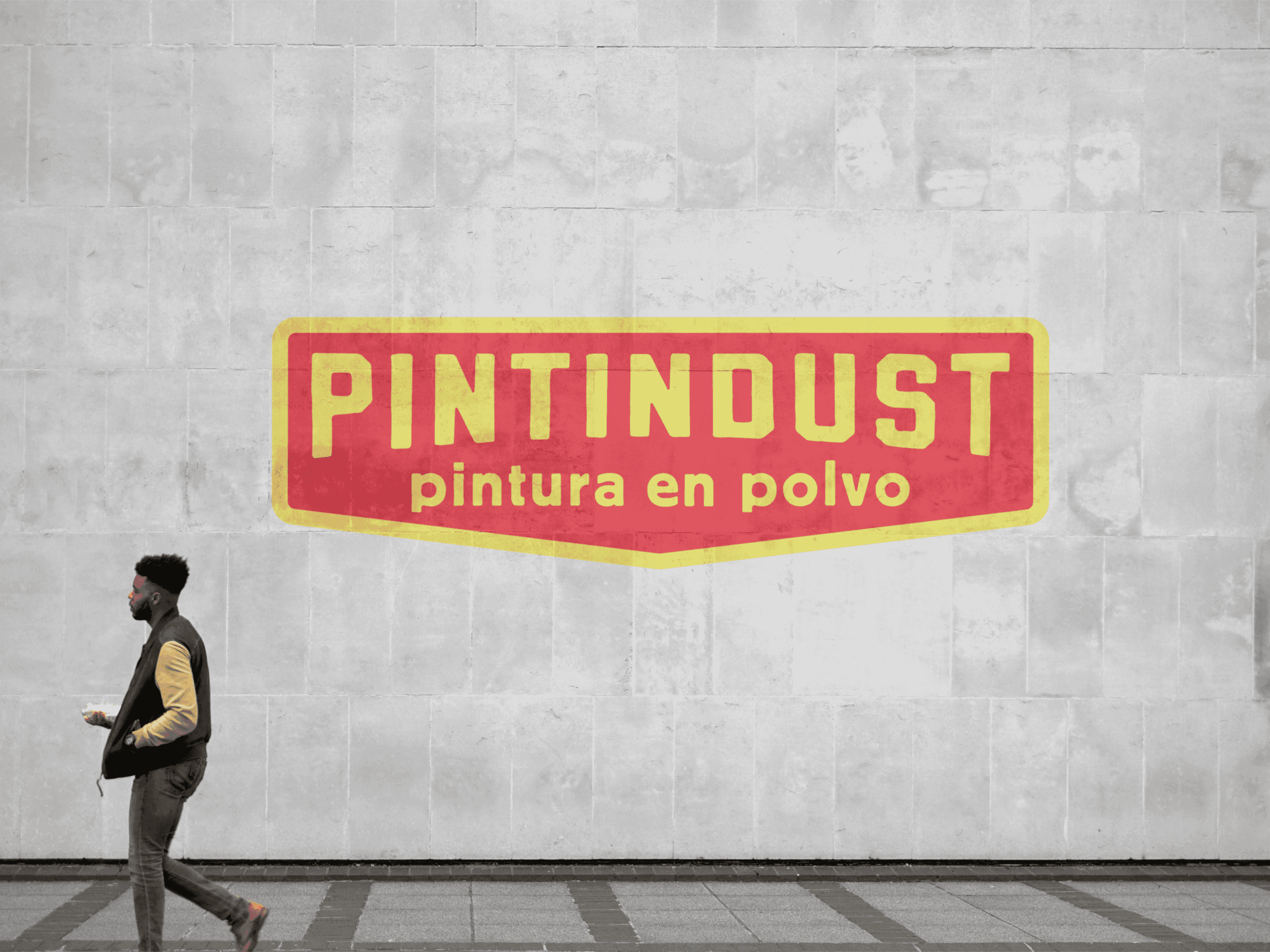 Логотип PINTINDUST на бетонній стіні в міському просторі. Повз іде чоловік, і бренд виглядає частиною реального міста.